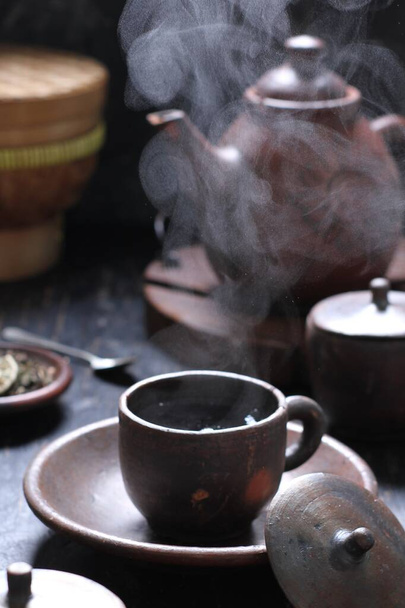 Tea is an aromatic beverage prepared by pouring hot or boiling water over cured or fresh leaves of Camellia sinensis, an evergreen shrub native to East Asia which probably originated in the borderlands of southwestern China and northern Myanmar.  - Foto, afbeelding