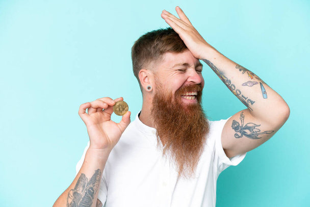Redhead man with long beard holding a Bitcoin isolated on blue background has realized something and intending the solution - Photo, Image