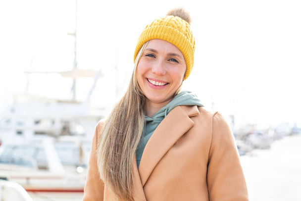 Young blonde woman wearing winter jacket at outdoors smiling a lot - Foto, imagen
