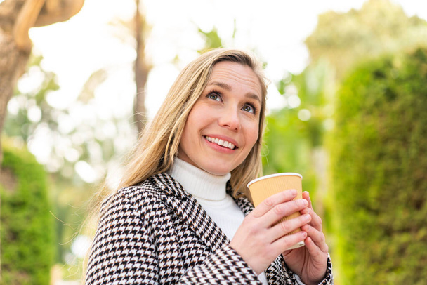 Young blonde woman holding a take away coffee at outdoors - 写真・画像