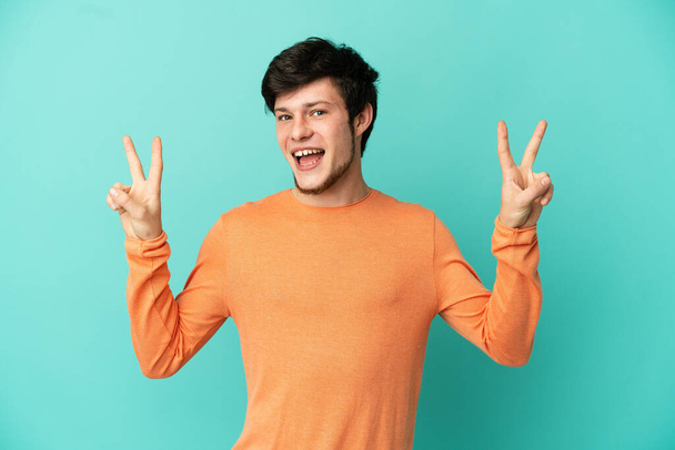 Young Russian man isolated on blue background showing victory sign with both hands - Photo, Image