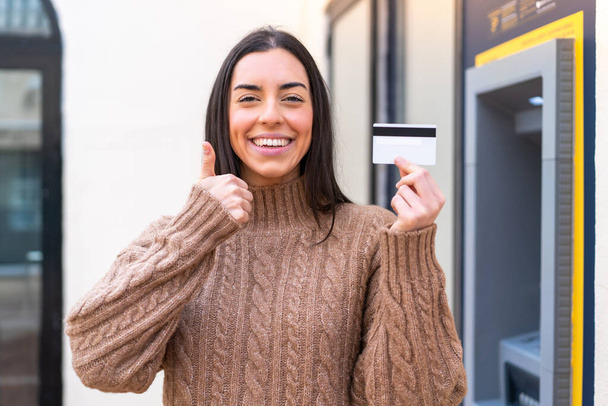 Fiatal nő kezében egy hitelkártya a szabadban hüvelykujjal felfelé, mert valami jó történt - Fotó, kép
