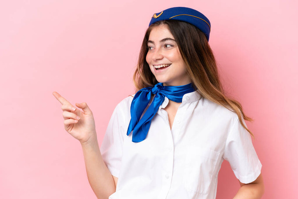 Letadlo letuška běloška žena izolované na růžovém pozadí ukazující prstem na stranu a prezentující produkt - Fotografie, Obrázek