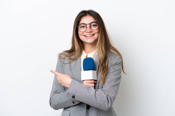Mujer joven presentadora de televisión caucásica aislada sobre fondo blanco apuntando hacia un lado para presentar un producto - Foto, Imagen