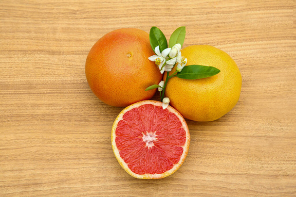 Fresh ripe grapefruits, flowers and green leaves on wooden table, top view - Foto, Bild