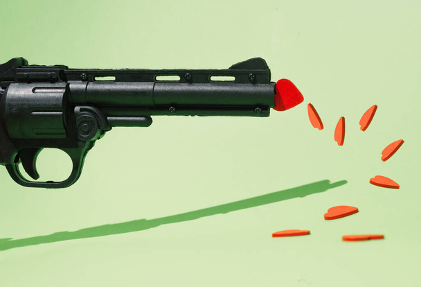 A gun and red hearts scattered on the floor. Pastel green background. Don't kill love. - 写真・画像