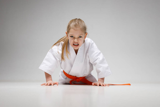 Push-ups of a strong little girl on a white background in a kimono, karate training. - Φωτογραφία, εικόνα