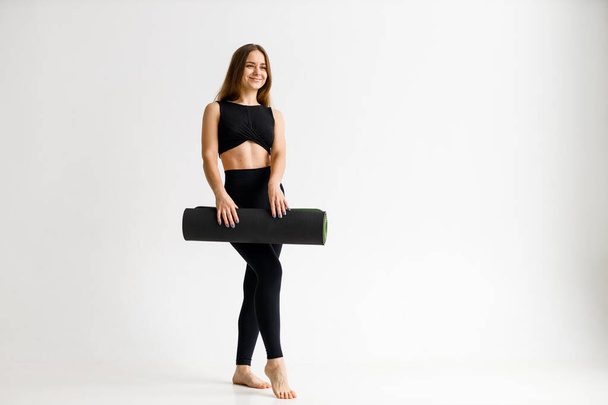 Young athletic woman with a mat in her hands in a white gym after a workout. - Photo, image