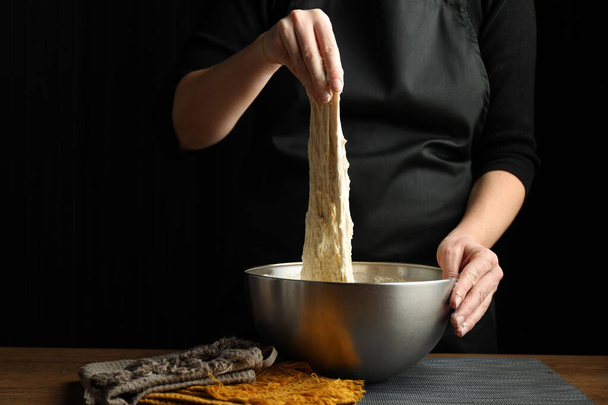 Kneading yeast dough, hands stretch wheat sourdough on a black background. - Zdjęcie, obraz