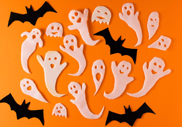 White ghosts and bat craft for Halloween party. Wrapping paper ghost on orange background top view. Cartoon creepy Whisper. DIY hand made. Set boo characters. - Foto, imagen