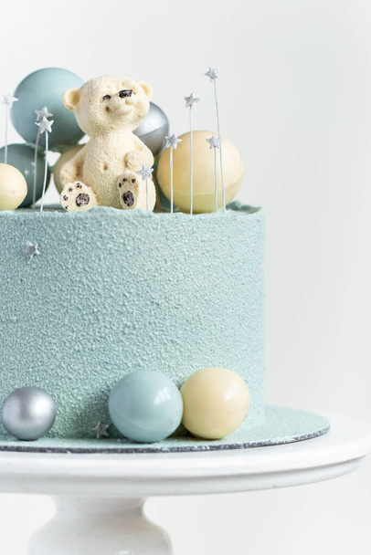 Cake with blue or turquoise velvet cream coating with teddy bear on top. Birthday cake for a little baby with chocolate turquoise and silver spheres on the white background. One year old celebration. - 写真・画像