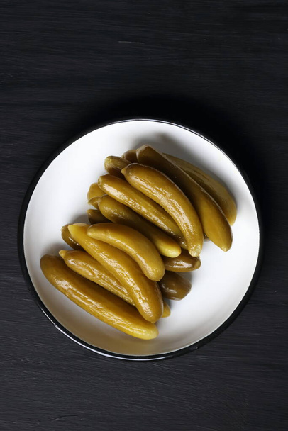 Cucumber pickle in a plate on a black background - Foto, afbeelding
