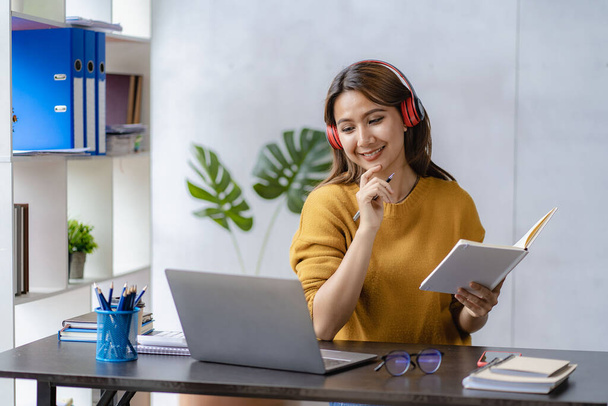 Mujer joven y feliz usando auriculares inalámbricos aprendiendo el idioma en línea escuchando conferencias viendo webinars escribiendo notas viendo portátil sentado en casa aprendizaje a distancia - Foto, Imagen