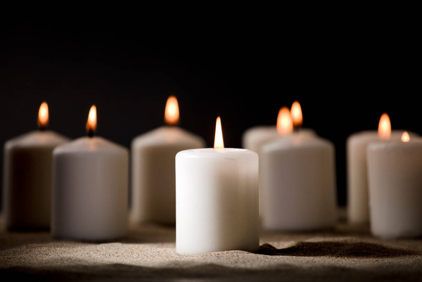 concepto de intimidación, compuesto por un grupo de velas encendidas, sobre arena con fondo negro nocturno - Foto, Imagen