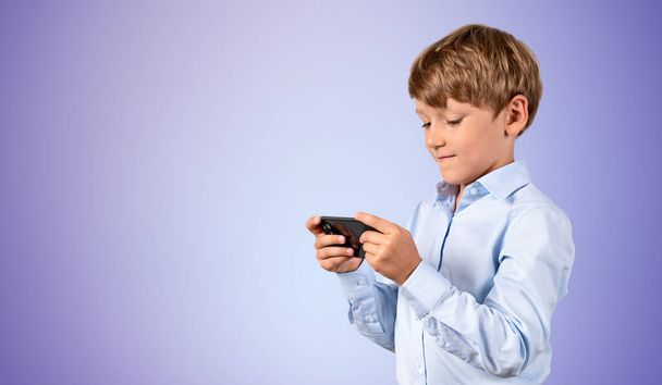 Portrait of serious little boy using smartphone over purple background. Concept of internet usage for education and joy. Mock up - Photo, Image