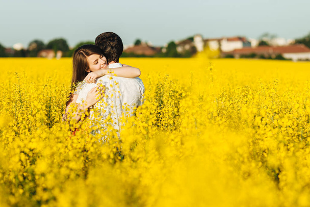 Passionate affectionate couple embrace each other, miss very much as haven`t seen for long time, spend wonderful summer day outdoor in yellow field. Romantic female and male hug with great love - Zdjęcie, obraz