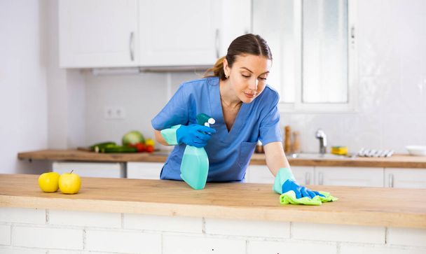 Professional cleaner wipes the table in the kitchen with a rag - Foto, afbeelding