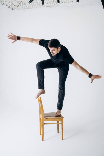 Guy in black T-shirt stands on chair and loses his balance - 写真・画像