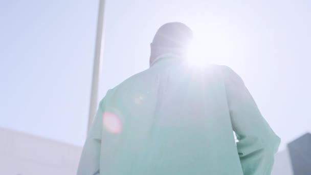 Back, flare and walking with a black man in the city from below for his morning commute on a blue sky. Urban, lifestyle and fashion with an african male outside for a walk in the town during summer. - Záběry, video