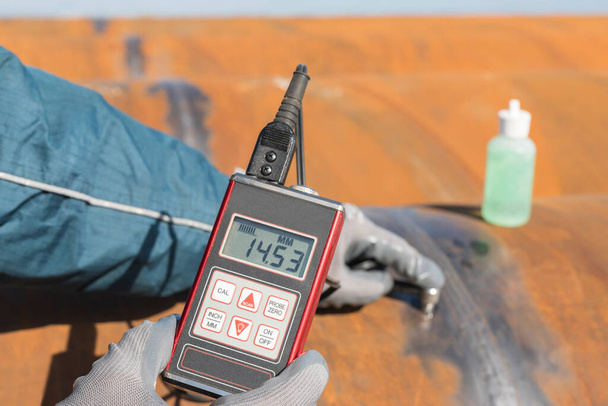 Inspector is measuring thickness of the pipe material from near to weld with a portable ultrasonic wall thickness measurement gauge. It is a method of performing non destructive measurement (gauging). - Foto, immagini
