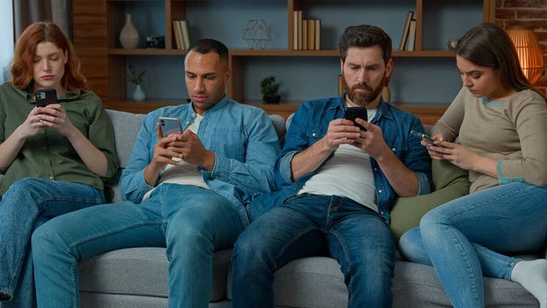 Орієнтовані чотири різноманітних афроамериканських американських кавказьких його друзі сидять на дивані у вітальні дивіться на мобільний екран разом телефонний гаджет інтернет залежні чоловіки жінки ігнорують один одного нудні зустрічі
 - Фото, зображення