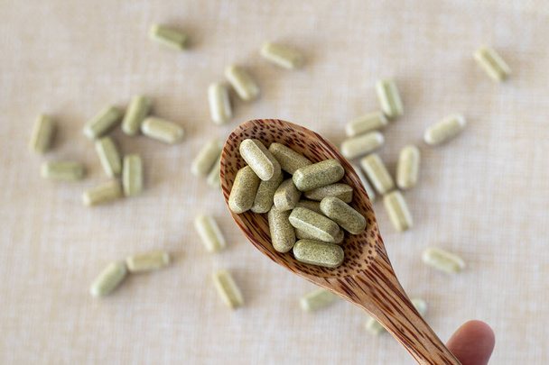 Vitamin aus Brokkoli-Sulforaphan in Kapseln in einem Holzlöffel auf beigem Hintergrund. Tabletten und Medikamente in grün. - Foto, Bild