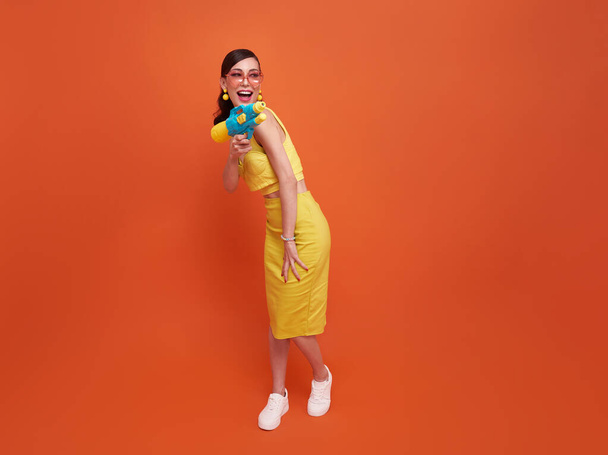 ソンクラン祭スタジオで水銃を持って旅する陽気な観光客の女性のコピースペースオレンジの背景. - 写真・画像