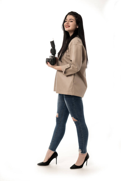 fotógrafa mujer tomando fotos en estudio sobre fondo blanco, usando jeans y chaqueta de cuero marrón. sesión de cámara fotográfica - Foto, Imagen