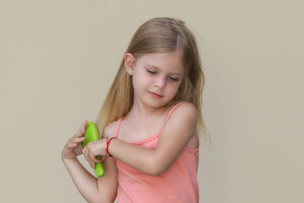 Candid portrait of cute little girl combing her long hair with detangler brush - Photo, Image