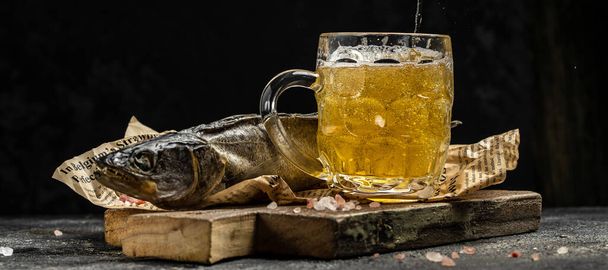 Mousse bière dans une tasse, poisson séché stockfish fond sombre. Concept de brasserie de bière. place pour le texte. - Photo, image