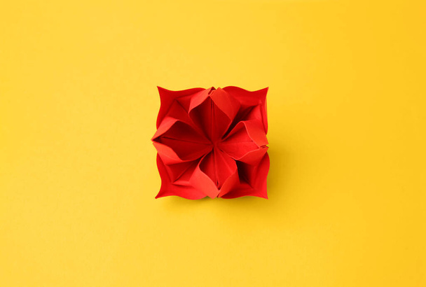 Origami art. Handmade red paper flower on yellow background, top view - Фото, изображение