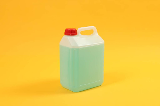 Plastic canister with green liquid on orange background - Foto, afbeelding