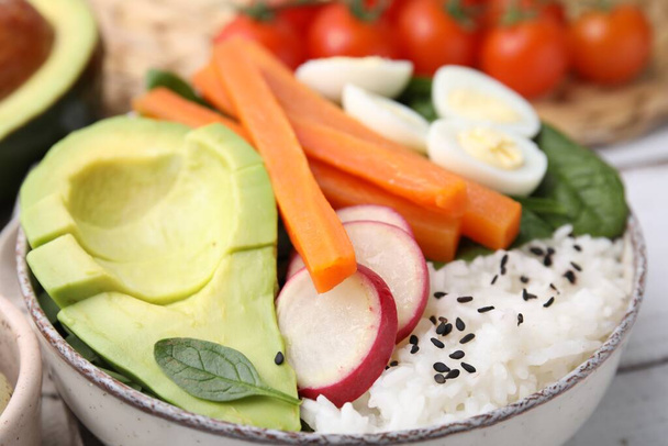 Delicious poke bowl with basil, eggs, avocado and vegetables on white wooden table, closeup - Fotó, kép
