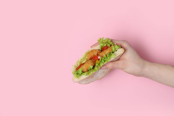 Woman holding delicious pita sandwich with fried fish, pepper, tomatoes and lettuce on pink background, closeup. Space for text - Foto, imagen