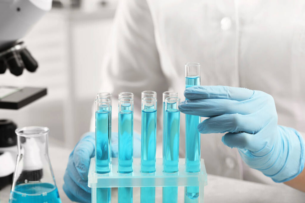 Scientist taking test tube with light blue liquid in laboratory, closeup - 写真・画像