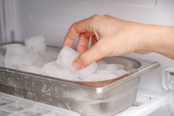 The girl takes frozen ice cubes from the freezer with her hand to prepare soft drinks. - Photo, Image