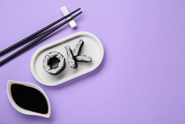 Palabra Ok hecha de rollos de sushi, palillos y salsa de soja sobre fondo violeta, puesta plana. Espacio para texto - Foto, imagen