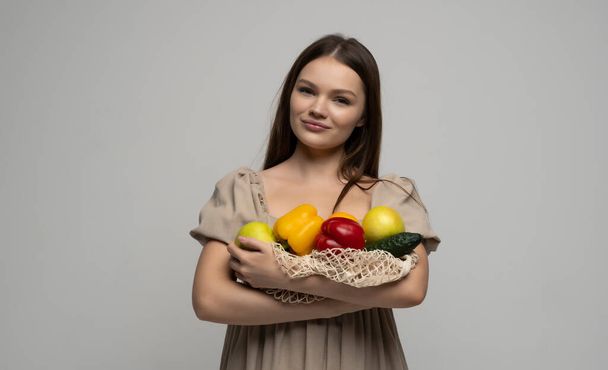 Beautiful attractive happy brunette woman holding mesh grocery bag with vegetables. Concept of no plastic. Zero waste, plastic free. Eco friendly concept. Sustainable lifestyle - Фото, зображення