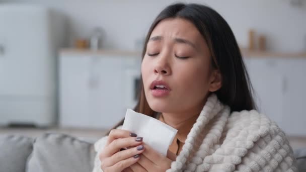 Sick Asian woman covered in blanket sneezing in paper napkin sneeze runny nose feel frozen cold unhealthy korean girl patient has covid symptom grippe nasal infectious disease health treatment at home - Imágenes, Vídeo