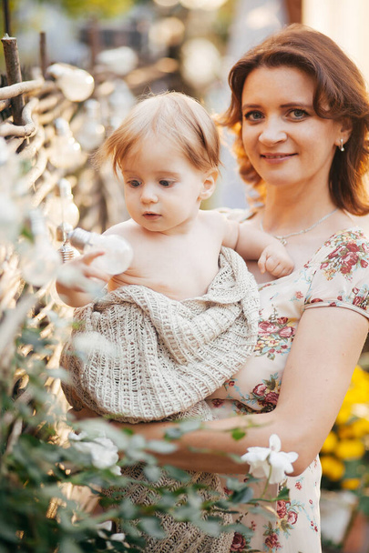 Молодая женщина держит своего маленького сына на руках в саду  - Фото, изображение