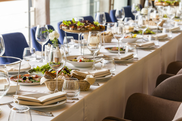 μεγάλο τραπέζι με τραπεζομάντηλο σερβιρισμένο με πιάτα με υφασμάτινες χαρτοπετσέτες με μαχαίρια και ποτήρια με φαγητό - Φωτογραφία, εικόνα