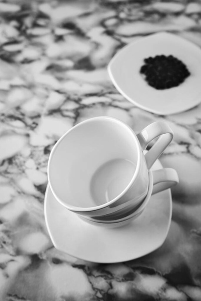 dva bílé hrnky kávy stojící jeden na druhé na bílém podšálku v černé a bílé, horní pohled - Fotografie, Obrázek