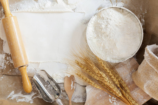 Flour in a bowl and wheat grains with wheat ears on the table, paper background In a rustic kitchen, top view - Foto, imagen
