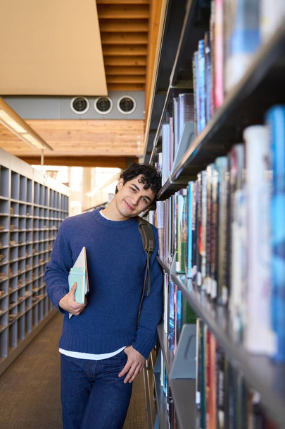 Yakışıklı Latin Amerikalı erkek öğrenci gülümsüyor, kameraya bakıyor, diploma projesi veya sınav hazırlıkları için üniversite kütüphanesini ziyaret ediyor. - İnsanlar. Eğitim. - Bilgi. Öğrenme - Fotoğraf, Görsel