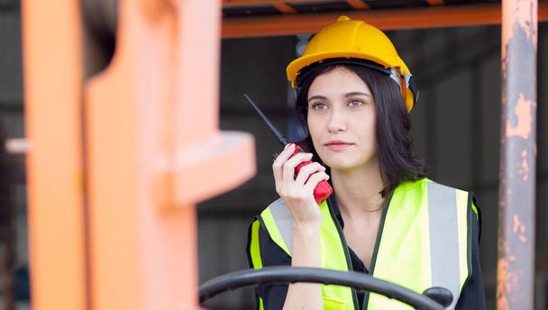 Young asian woman is foreman using radio for communication while driving forklift at distribution warehouse, engineer working and shipping container at factory, cargo and logistic, industry concept. - Foto, immagini