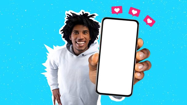 Cool όμορφος νεαρός μαύρος τύπος σε λευκό hoodie δείχνει κινητό τηλέφωνο με λευκή οθόνη στην κάμερα, εικονίδια καρδιά πάνω από το smartphone, δείχνει ωραία χρονολόγηση app, πολύχρωμο φόντο, mockup, κολάζ - Φωτογραφία, εικόνα
