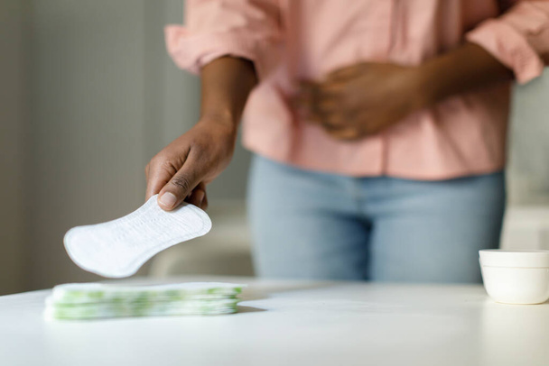 Femme afro-américaine ressentant de la douleur pendant le cycle menstruel et prenant un tampon hygiénique quotidien de la table, foyer sélectif, gros plan, espace libre - Photo, image