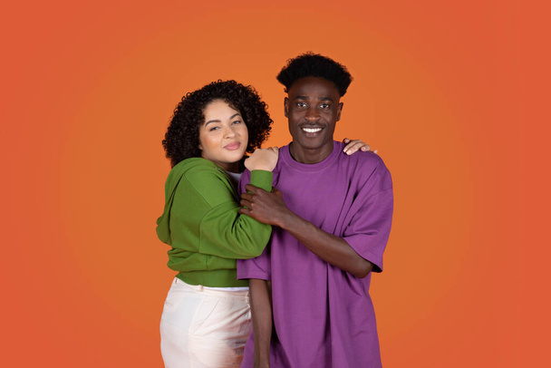 Schöne glücklich liebende junge miltiracial Paar hübsche mollige hispanische Frau mit lockigem Haar und schöner schwarzer Kerl umarmt auf bunten Studiohintergrund, lächelnd in die Kamera. Beziehungskonzept - Foto, Bild