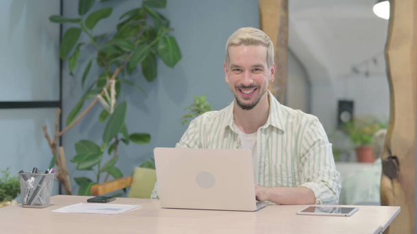 Сучасна молода людина посміхається в камері, користуючись ноутбуком - Фото, зображення