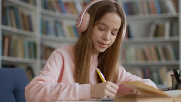 Online oktatás. Laptop pov portré fiatal nő hallgató fülhallgató nézi webinar és jegyzetel, tanul campus könyvtár belső - Felvétel, videó